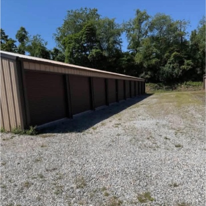 Row of brown roll-up storage unit doors along the gravel drive at Penny Lane Mini Storage